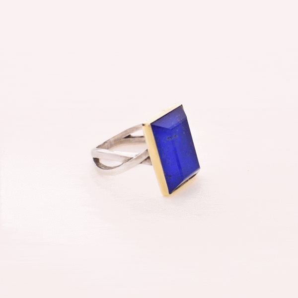 Handmade sterling silver and gold ring with doublet made of crystal quartz and lapis lazuli gemstones, in a parallelogram shape. The band of the ring is made of sterling silver and the outline of the bezel is made of 18 carats gold. The doublet consists of two layers of stones. The upper stone is crystal quartz and the stone at the bottom is lapis lazuli.