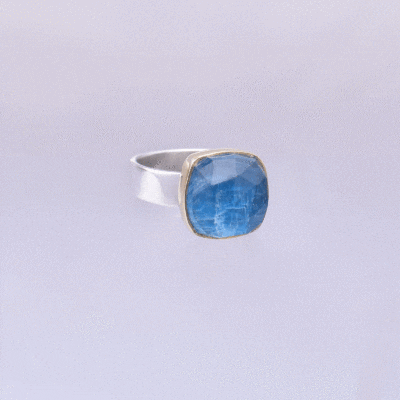 Handmade sterling silver and 18k gold ring with doublet made of natural crystal quartz and apatite gemstones, in a square shape. The band of the ring is made of sterling silver and the outline of the bezel is made of 18 carats gold. The doublet consists of two layers of stones. The upper stone is faceted crystal quartz and the stone at the bottom is apatite. Buy online shop.