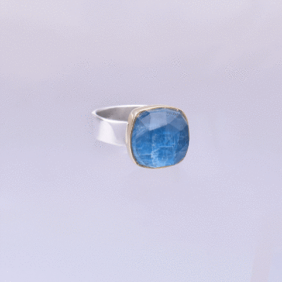 Handmade sterling silver and 18k gold ring with doublet made of natural crystal quartz and apatite gemstones, in a square shape. The band of the ring is made of sterling silver and the outline of the bezel is made of 18 carats gold. The doublet consists of two layers of stones. The upper stone is faceted crystal quartz and the stone at the bottom is apatite. Buy online shop.