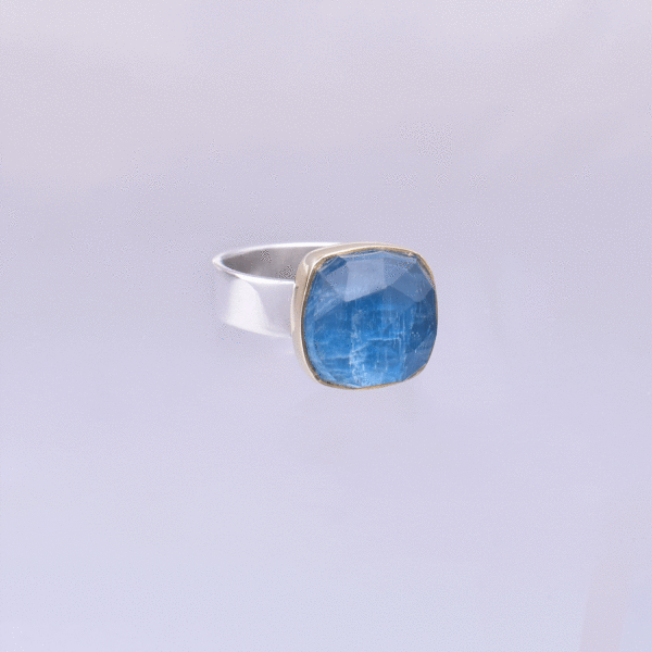 Handmade sterling silver and 18k gold ring with doublet made of natural crystal quartz and apatite gemstones, in a square shape. The band of the ring is made of sterling silver and the outline of the bezel is made of 18 carats gold. The doublet consists of two layers of stones. The upper stone is faceted crystal quartz and the stone at the bottom is apatite. Buy online shop.