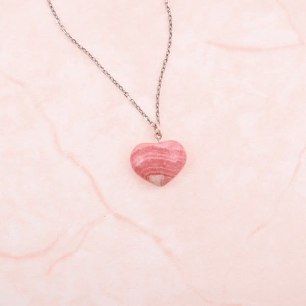 Handcrafted heart-shaped pendant made from natural rhodochrosite gemstone. The pendant is threaded on a handmade sterling silver chain.