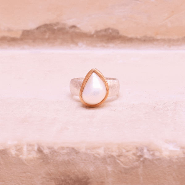 Handmade ring made of sterling silver and natural, teardrop shaped pearl. The ring has textured band and gold plated bezel. 