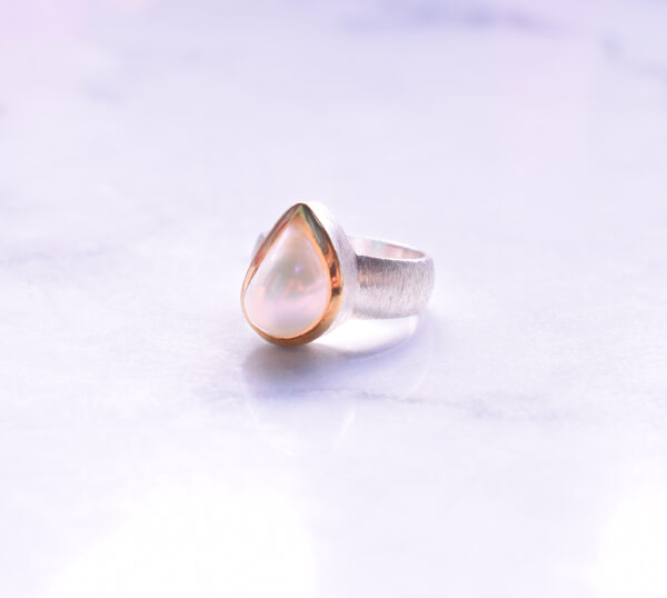 Handmade ring made of sterling silver and natural, teardrop shaped pearl. The ring has textured band and gold plated bezel. 